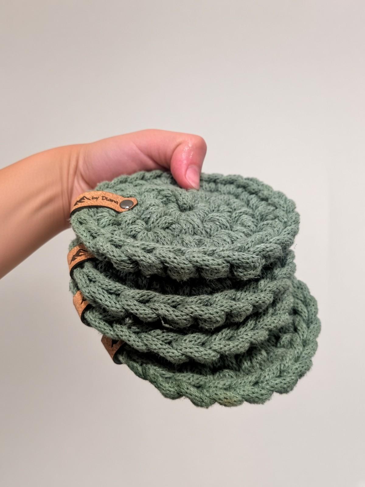Hand holding a stack of sage green handmade crochet coasters