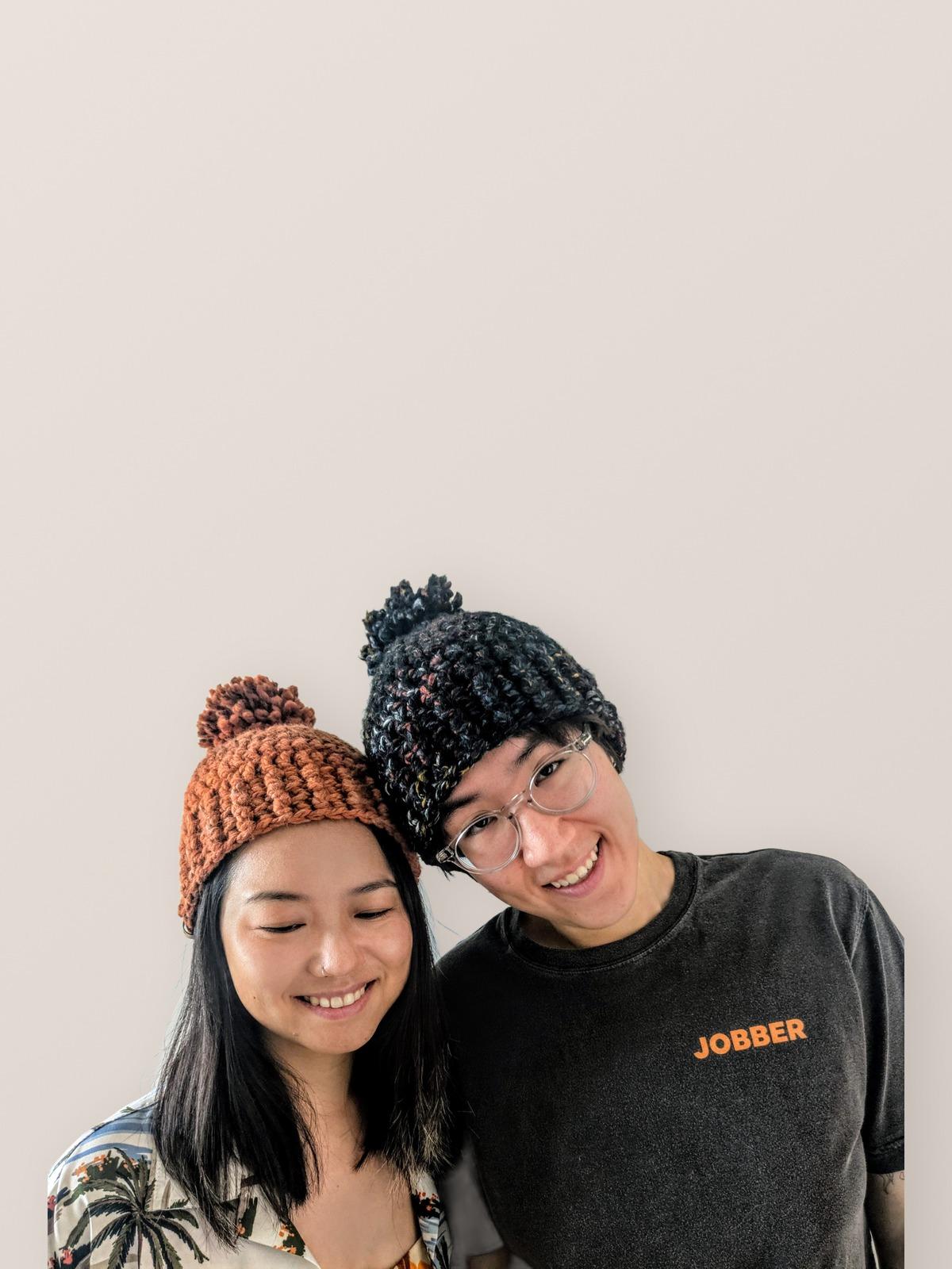 Two people wearing handmade crochet pom-pom beanies